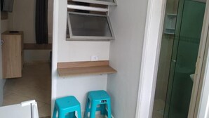 A room with a kitchenette, a shower area, and a small seating area with two stools.