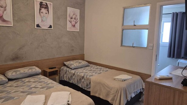 A hotel room with two beds, a desk, and a window.