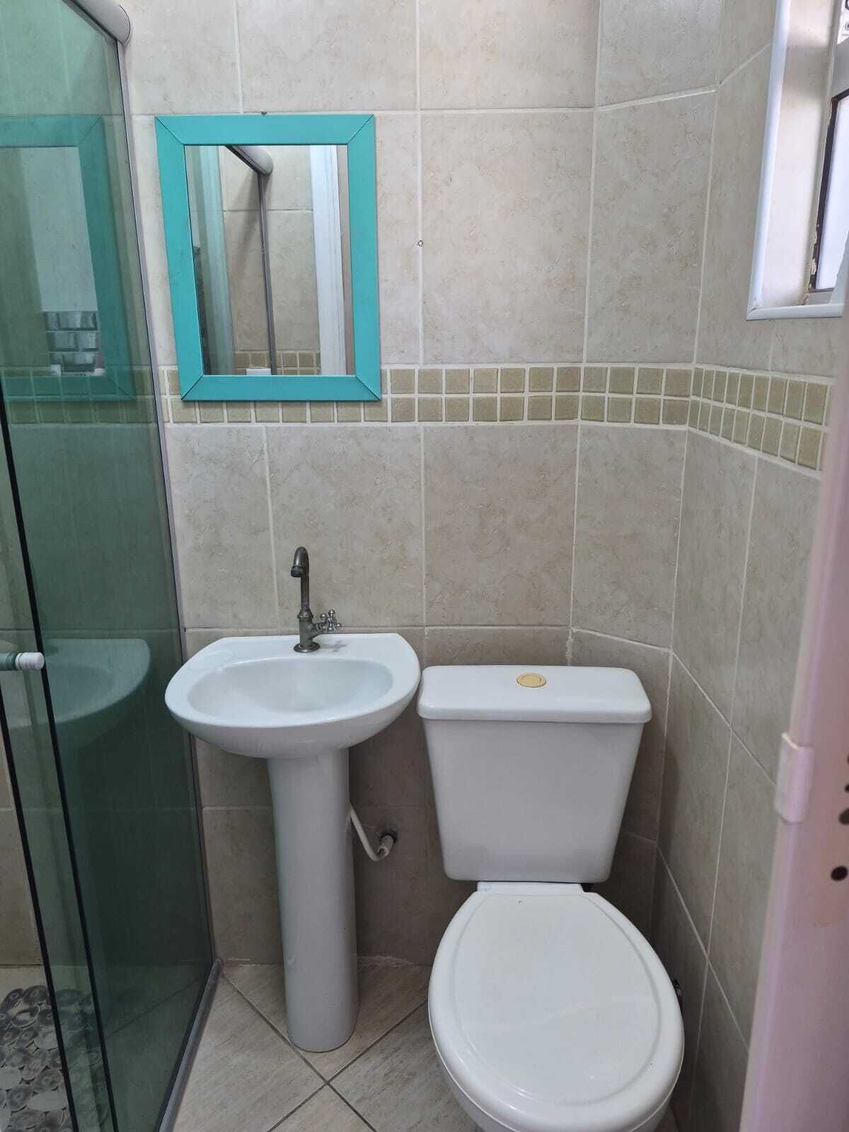 Une salle de bain avec une douche à parois de verre, un lavabo sur colonne, des toilettes et un miroir avec un cadre de couleur turquoise.