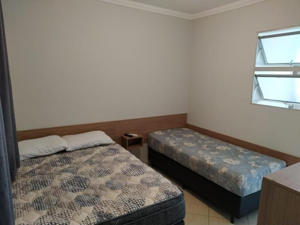 A bedroom with a large bed, a smaller bed, a nightstand, and a window.