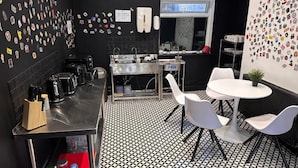 A modern kitchen with a black and white patterned floor, stainless steel appliances, and white chairs around a small table. - Digz Hotel (Middlesbrough)