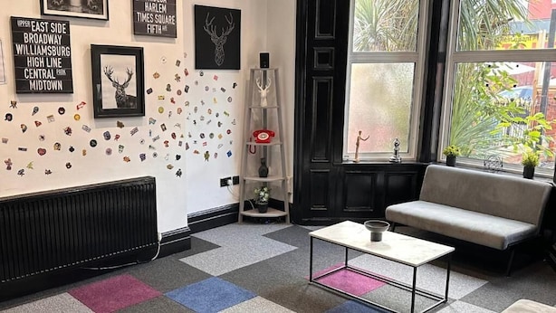 A room with a black radiator, a grey sofa, a white coffee table, and a window with plants. - Digz Hotel (Middlesbrough)
