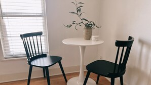 Dos sillas negras y una mesa blanca en una habitación con suelo de madera y una ventana con persianas.