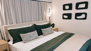 Un dormitorio ordenado con cama, almohadas, una mesita de noche y un aplique de pared.