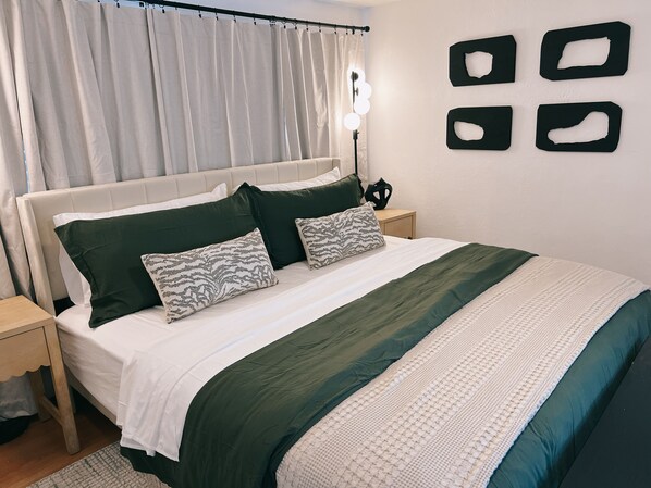 Un dormitorio ordenado con cama, almohadas, una mesita de noche y un aplique de pared.