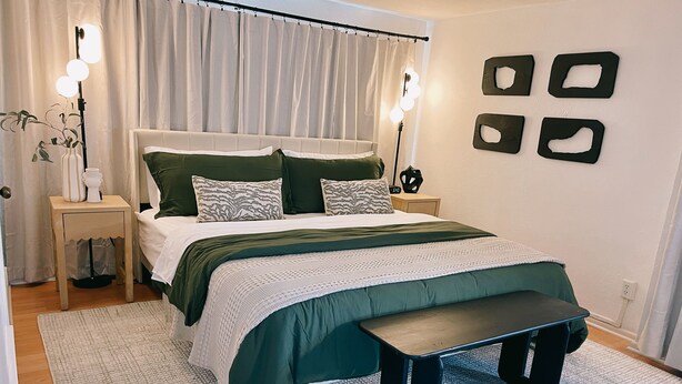 Un dormitorio ordenado con cama, mesitas de noche, un banco y cuadros en la pared.