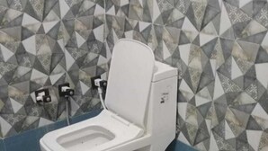 A bathroom with a white toilet, a blue wall, and a patterned wall behind the toilet. - HOLKAR SEVA SADAN (Mathura)