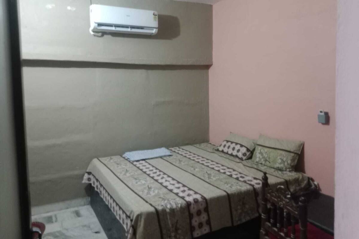 Una habitación pequeña con cama individual, una colcha estampada, aire acondicionado de pared y una pared lisa.