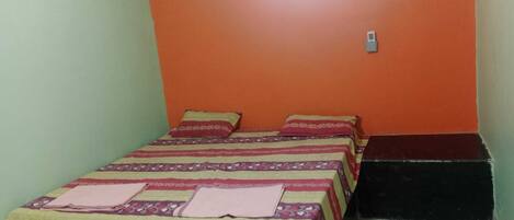 A small, single-bed room with a patterned bedspread, an air conditioning unit on the wall, and a tiled floor.