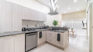 A modern kitchen with light wood cabinets, a stainless steel dishwasher, granite countertops, and a central island with a sink. - 2 BD Suite w/ Balcony, Gym, Rooftop Pool, Jacuzzi (Playa del Carmen)