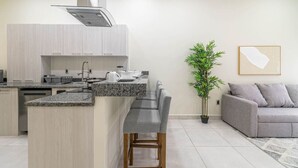 A modern kitchen with a central island, bar stools, and a grey sofa in a living area. - 2 BD Suite w/ Balcony, Gym, Rooftop Pool, Jacuzzi (Playa del Carmen)