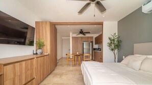 Une chambre à coucher moderne avec un grand lit, des meubles en bois, un ventilateur de plafond et une vue sur la cuisine.