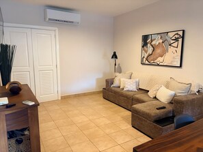 Un soggiorno con un divano marrone, un tavolino, una lampada e un quadro appeso al muro.