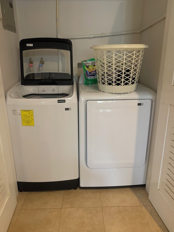 A compact laundry area with a front-loading washer and dryer, a white basket on the dryer, and a green detergent bag.