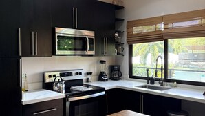 A modern kitchen with dark cabinets, stainless steel appliances, a wooden countertop, and a window with a view of greenery. - Coco Beach Costa Rica, 2 Bedrm 2 Bath condo with beautiful outdoor space (Guanacaste Province)