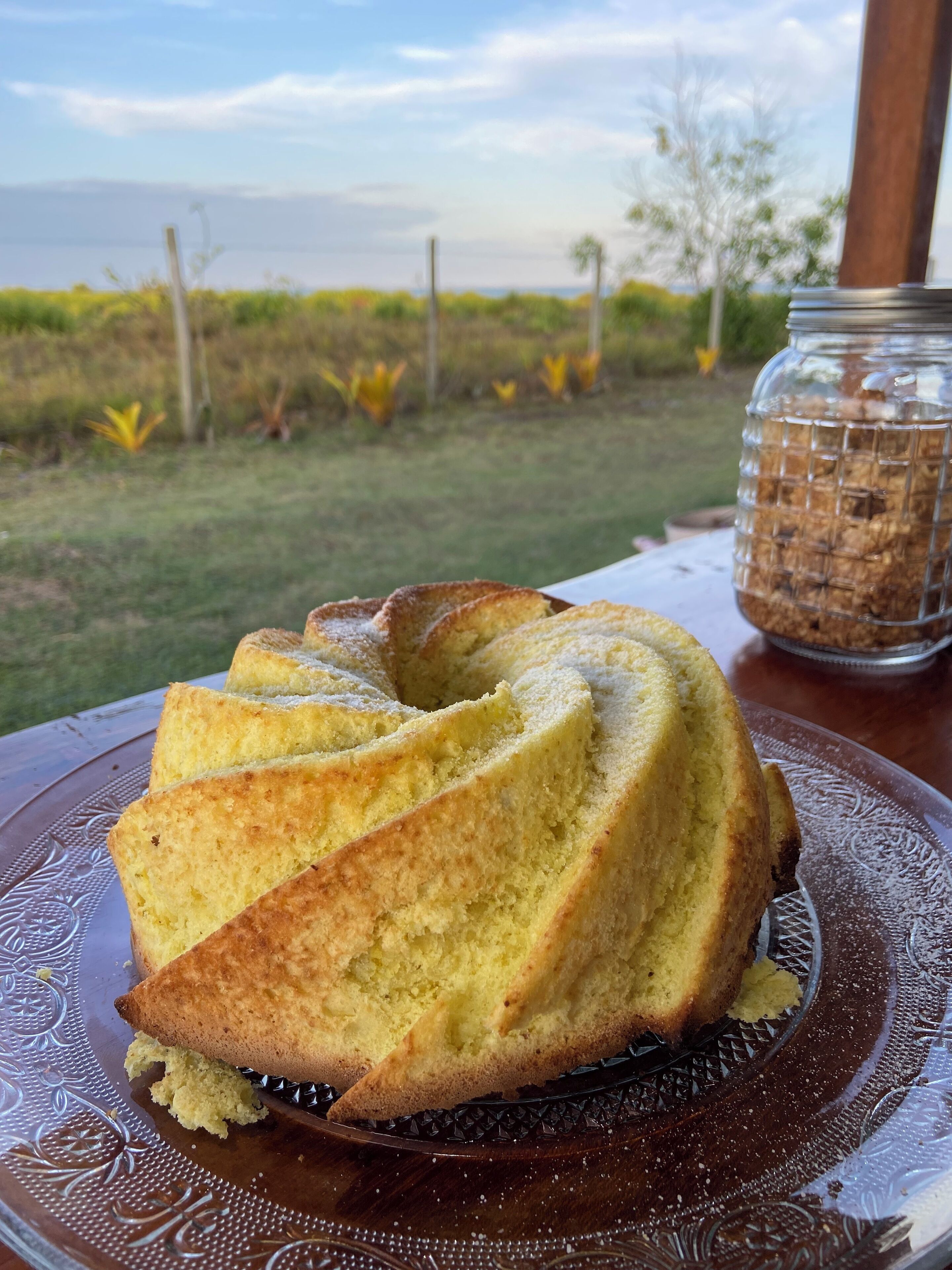A bundt cake on a decorative plate with a jar of granola in the background.