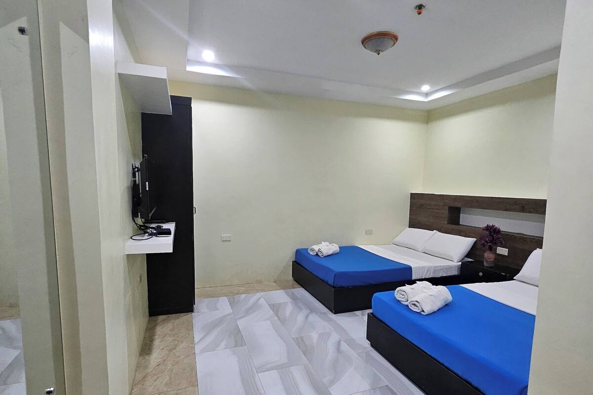 A hotel room with two beds, a small desk with a TV, and a bathroom visible through an open door.