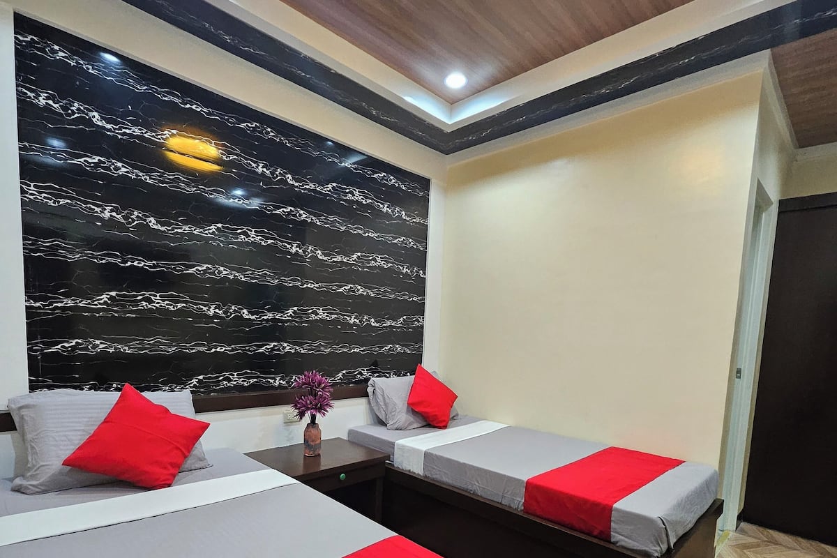 A modern hotel room with two beds, each with red and grey bedding, a marble-patterned wall, and a wooden floor.