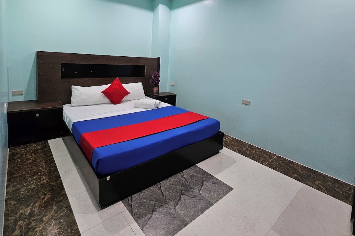 A bedroom with a bed, nightstands, a ceiling light, and a green light fixture.