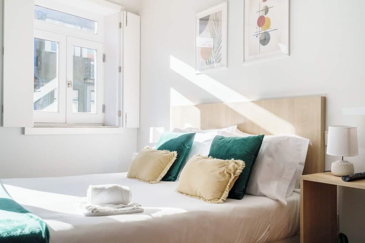 A hotel room with a bed, pillows, a bedside table with a lamp, and artwork on the wall.