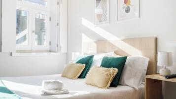 Una habitación de hotel con una cama, almohadas, una mesita de noche con lámpara y una obra de arte en la pared.