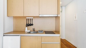 A compact kitchen with wooden cabinets, a stainless steel sink, and a small countertop. - Bellu Studios & Suites   (Braga)