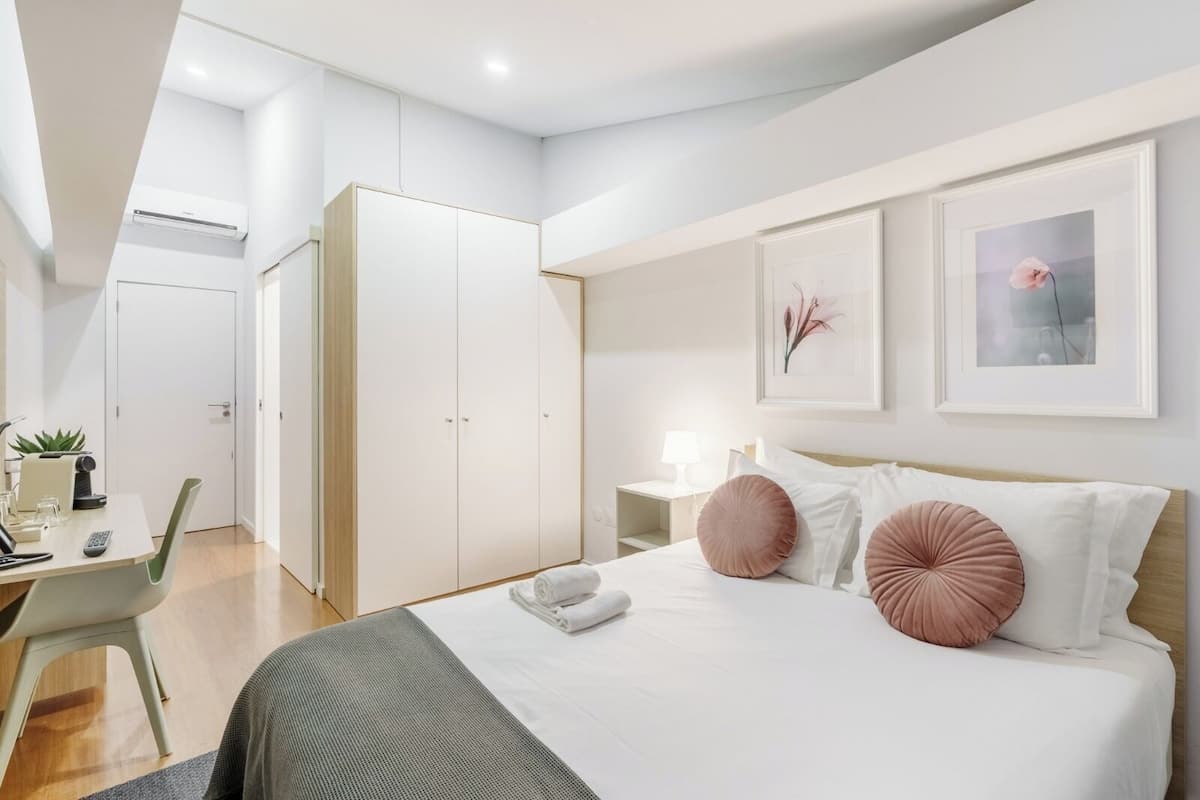A modern bedroom with a bed, bedside tables, a desk, and a wardrobe.