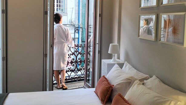 A hotel room with a bed, a nightstand, a lamp, and a balcony door. - Bellu Studios & Suites   (Braga)