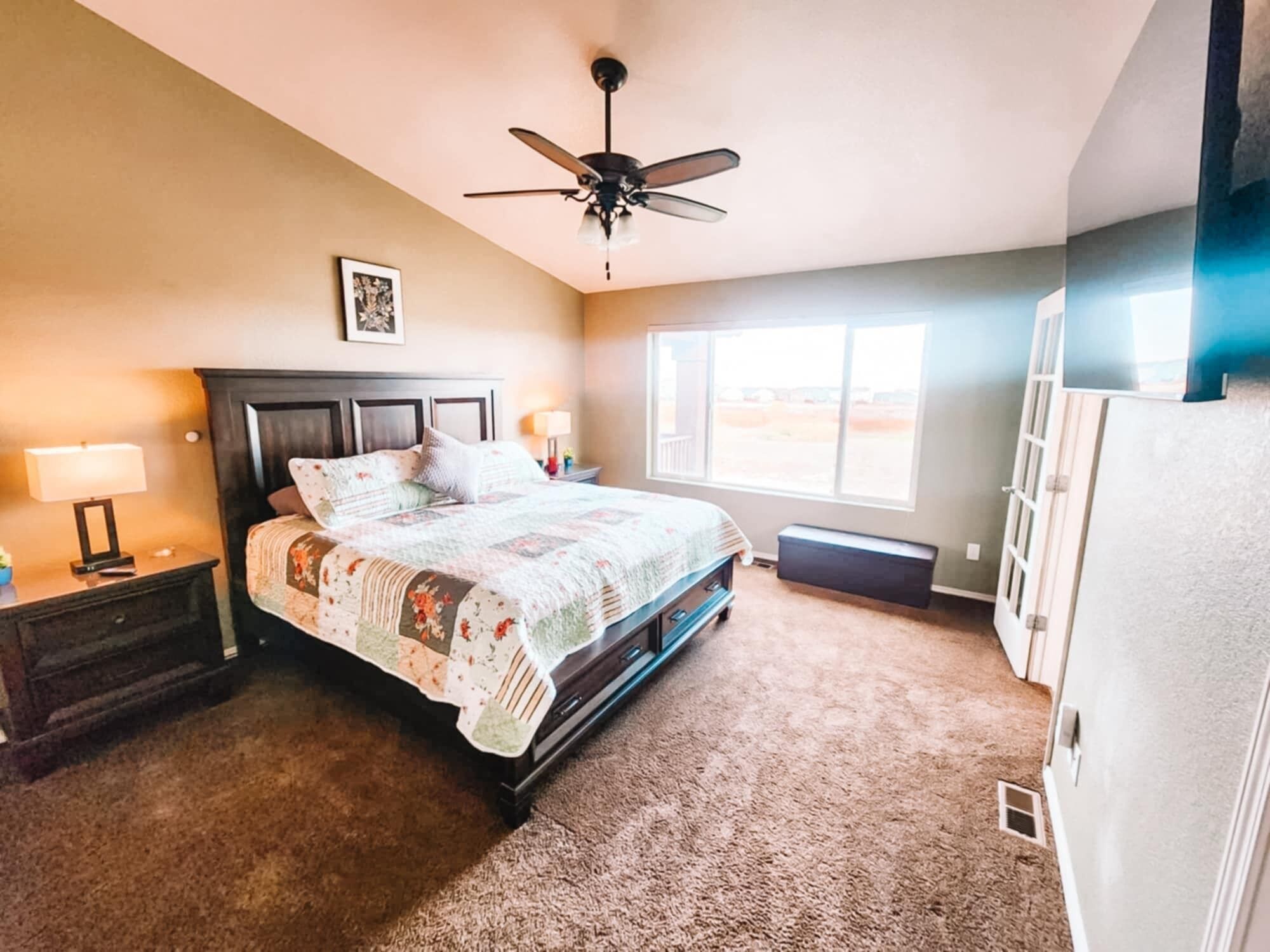 Une chambre à coucher avec un lit, un ventilateur de plafond, une fenêtre et une table de chevet avec une lampe.