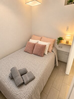 A neatly made bed with patterned bedding, a bedside lamp, and a small shelf with a plant.