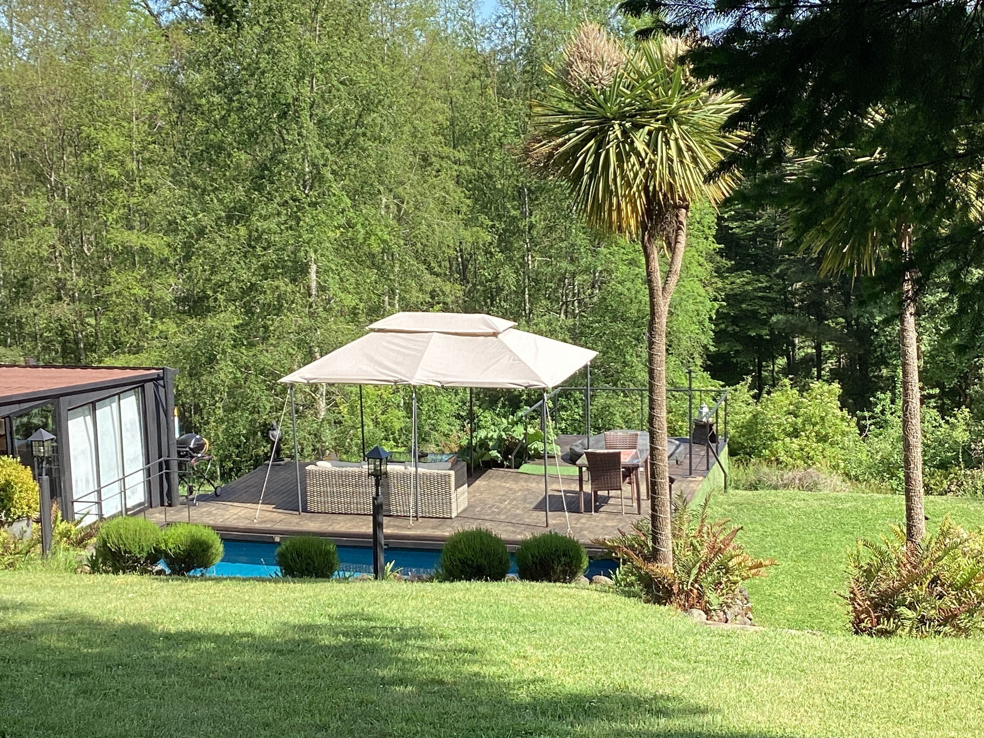 Un jardin avec une piscine, un patio couvert et une petite terrasse.