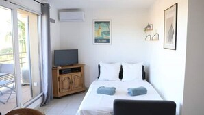 Ett hotellrum med en säng, en tv-apparat på ett träskåp, en affisch på väggen och en skjutdörr i glas som leder ut till utsidan.