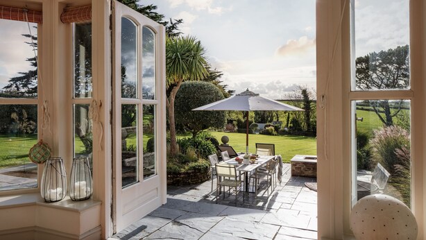 A conservatory with a view of a garden, a patio with a table and chairs, and a decorative vase. - Shalmar Hollow - Rock - sleeps up to 12 - perfect for family groups (Rock)
