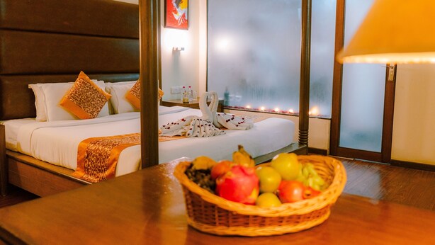 Une chambre d’hôtel avec un lit, un panier de fruits sur la table et une grande fenêtre avec du verre dépoli.