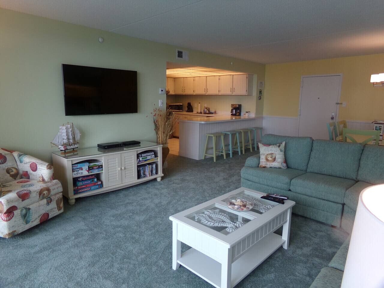 Un salon avec un canapé, une table basse, une bibliothèque, un téléviseur et, au fond, un coin cuisine.