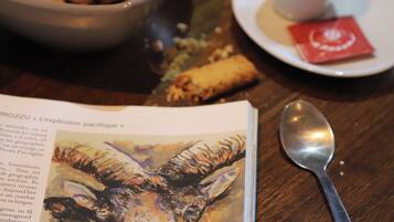 A table with a bowl of croquettes, a cup of tea, a spoon, and a book with a painting on the cover.