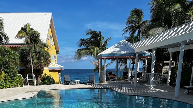 Ein Poolbereich mit Liegestühlen, einer überdachten Sitzecke und Blick auf das Meer.