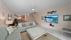 Ein Wohnzimmer mit einer Couch, einem Couchtisch und einem Fernseher. Eine Treppe führt zu einer weiteren Ebene.