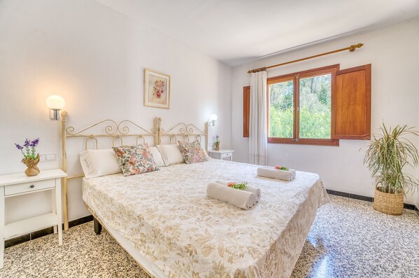 Une chambre à coucher comprenant un lit, des tables de chevet, une fenêtre avec des rideaux et un tableau accroché au mur.