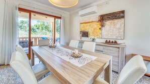 A dining area with a wooden table, white chairs, and a pendant light. - House in Alcudia Tacaritx with pool near the sea (Alcúdia)