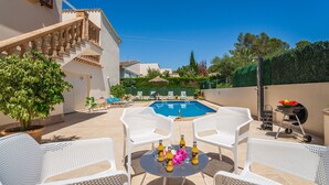A pool area with white outdoor furniture, a table with bottles, and a clear blue sky. - House in Alcudia Tacaritx with pool near the sea (Alcúdia)