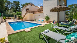 A swimming pool with lounge chairs and a small table with drinks, surrounded by a well-maintained lawn and a building with a balcony. - House in Alcudia Tacaritx with pool near the sea (Alcúdia)