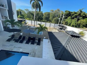 A modern hotel with a rooftop pool, outdoor seating, and lush greenery.