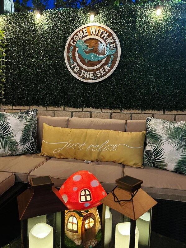 A cozy outdoor seating area with a round sign that reads "COME WITH ME TO THE SEA" and a cushion with the text "Just relax". - Charming home near the beach, downtown and main golf courses. (Myrtle Beach)