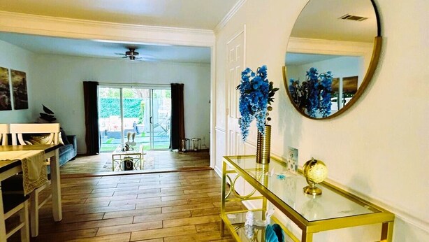 Um corredor amplo com piso de madeira, uma mesa de console de vidro com objetos decorativos e um espelho redondo na parede.
