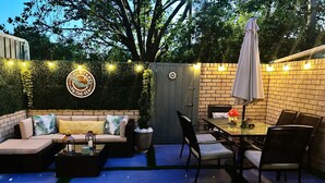 Um alpendre externo com sofá, cadeiras, mesa e luzes de cordão.