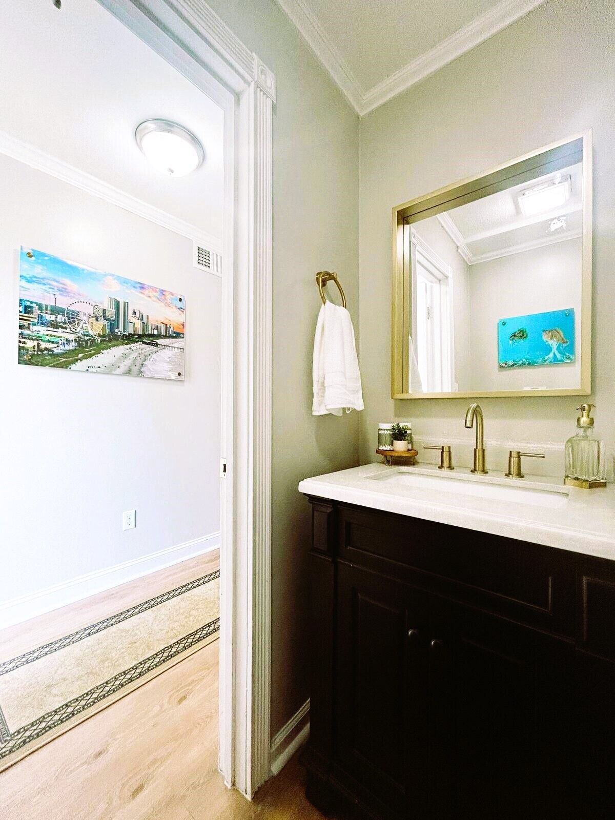Une salle de bain avec un grand miroir, un lavabo blanc et une serviette suspendue à un porte-serviettes doré.