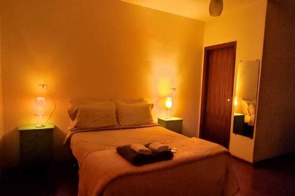 Ein Hotelzimmer mit Bett, Nachttischlampen, einer Holztür und einem kleinen Tisch mit Stuhl.