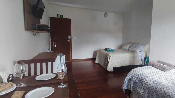 Ein Hotelzimmer mit einem Holzespeisetisch, gedeckt für zwei Personen, einem Bett mit gestreiftem Überwurf und einem an der Wand befestigten Fernseher.