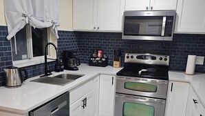 Una cocina moderna con armarios blancos, un lavavajillas de acero inoxidable, un horno doble, un microondas y una cafetera.